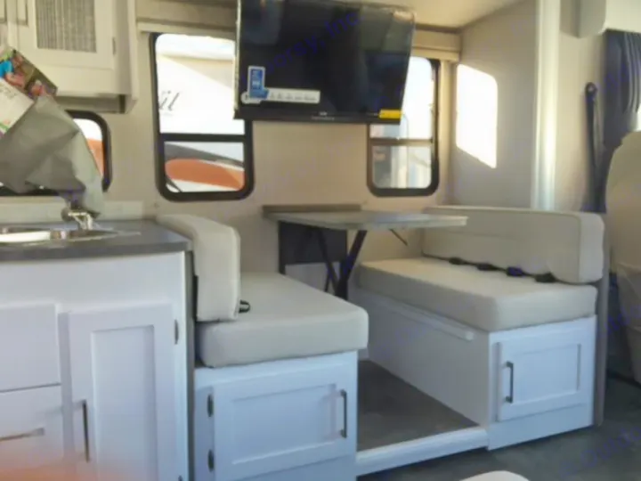 This RV rental interior features a bright dinette with a TV, facing a compact kitchen sink area. Ideal for road trips.. Forest River Coachmen Pursuit 2022