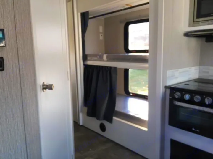 RV rental interior: bunk beds with windows, alongside a compact kitchen with an oven, microwave, and tile backsplash.. Forest River Coachmen Pursuit 2022