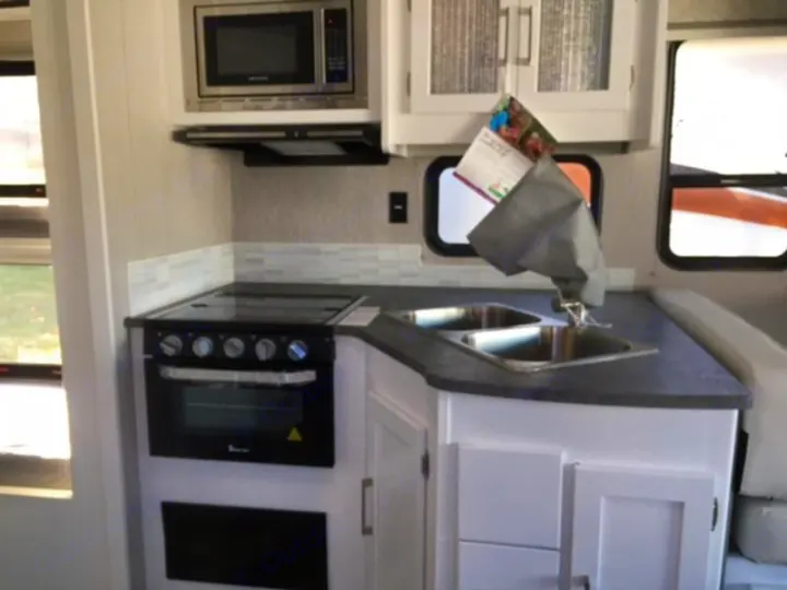 Inside an RV rental: a well-equipped kitchen with microwave, stove/oven, double sink, and cabinets for your travels.. Forest River Coachmen Pursuit 2022