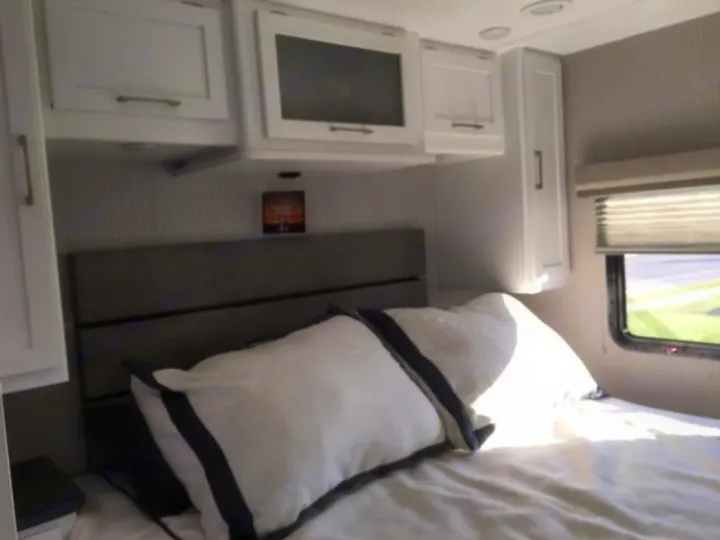 Experience comfort in this RV rental bedroom: a cozy bed, white overhead cabinets, and a window bringing in light.. Forest River Coachmen Pursuit 2022
