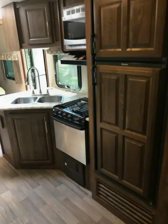 An RV rental kitchen with a dual sink, stove, microwave, and integrated refrigerator. Ready for your next journey!. Keystone Cougar Half-Ton 2017