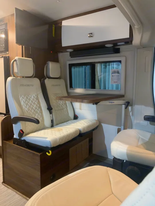 Explore this modern RV rental interior! Features cream seating, an adjustable table, TV, and microwave. Compact comfort for adventures.. Winnebago Travato 2022