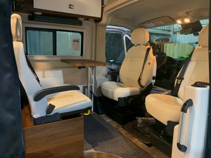 Explore this RV rental's interior: cream swiveling front seats, a rear bench, wood floor, and a compact table.. Winnebago Travato 2022