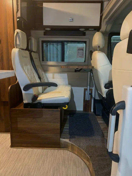 Bright RV rental interior with cream passenger seats, wood accents, and a movable table setup.. Winnebago Travato 2022