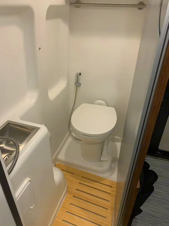 RV rental: a compact wet bath, featuring a toilet, sink with integrated shower, and wooden floor.. Winnebago Travato 2022