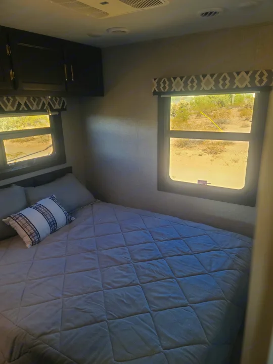 RV rental bedroom featuring a quilted bed, windows with a desert view, overhead cabinets, and air vents.. Entegra Vision 29F 2022