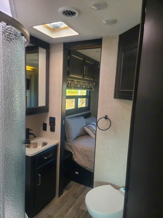 This RV rental offers a well-designed interior, featuring a bathroom with a sink and frosted glass shower, leading to a cozy bedroom.. Entegra Vision 29F 2022