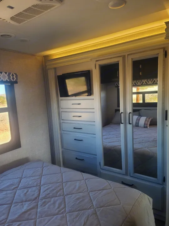 Inside an RV rental: a compact bedroom features a bed, mirrored wardrobe, TV, and storage drawers.. Entegra Vision 29F 2022