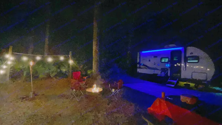 Nighttime at a lit-up RV rental campsite: blue-lit RV, warm string lights, and a cozy campfire.. Forest River Cherokee Wolf Pup Black Label 2021