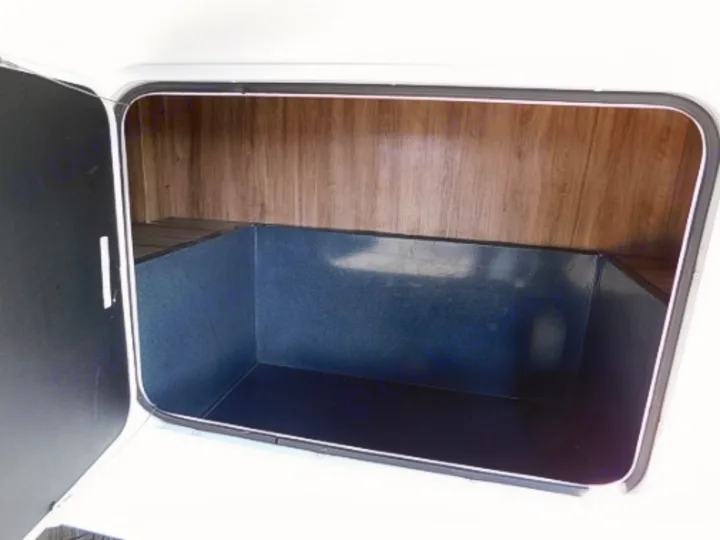 Open exterior storage bay of an RV rental, showing the lined interior and wood-paneled back wall for gear.. Entegra Coach Odyssey 2019