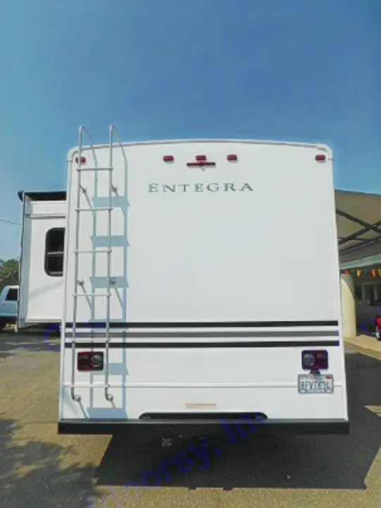 Rear view of a white Entegra RV rental, showing a ladder on the left, taillights, and an extended slide-out.. Entegra Coach Odyssey 2019