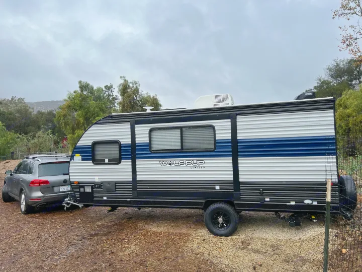 Grey SUV towing a striped Wolf Pup Limited travel trailer, parked on a dirt lot. Ready for an RV rental adventure.. Forest River Cherokee Wolf Pup 2022