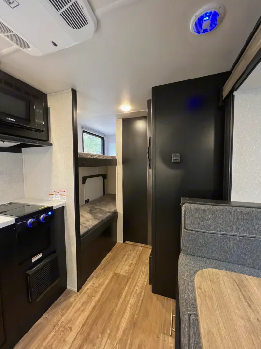 Inside an rv rental: functional kitchenette, cozy bunk beds, and comfy seating with a table, all under ceiling AC and blue lights.. Forest River Cherokee Wolf Pup 2022