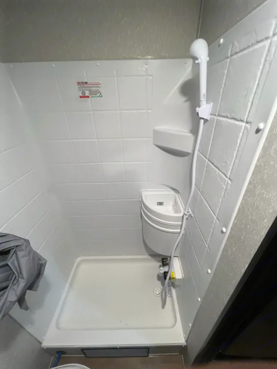 Inside an RV rental: a practical, compact white shower stall with a small sink and handheld showerhead.. Forest River Cherokee Wolf Pup 2022
