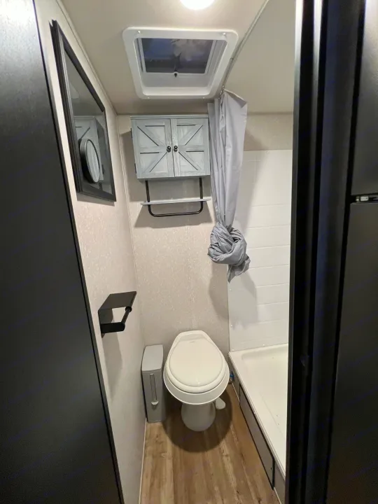 Compact RV rental bathroom, featuring a toilet, shower, and stylish storage cabinet for efficient space usage.. Forest River Cherokee Wolf Pup 2022