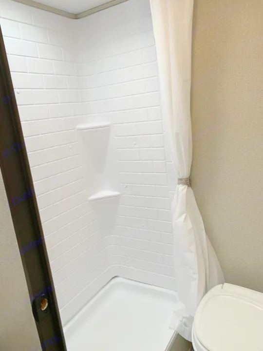 RV rental compact white shower with faux-tile walls and corner shelves. White shower curtain and toilet visible on right.. Prime Time Avenger 2021
