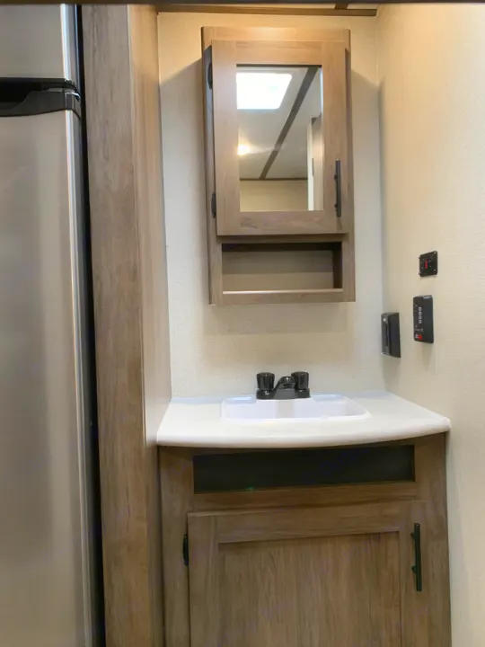 RV rental interior: Compact bathroom vanity with sink, medicine cabinet, and storage, next to the refrigerator.. Prime Time Avenger 2021