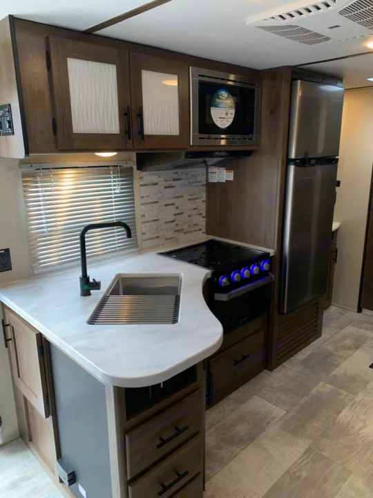 A spacious, modern RV rental kitchen with full appliances: sink, stove, microwave, fridge, and ample storage cabinets.. Prime Time Avenger 2021