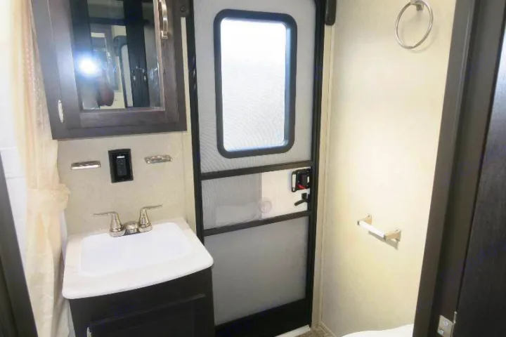 Bright RV rental bathroom with vanity, sink, mirrored cabinet, and a functional RV door.. Palomino Puma 2018