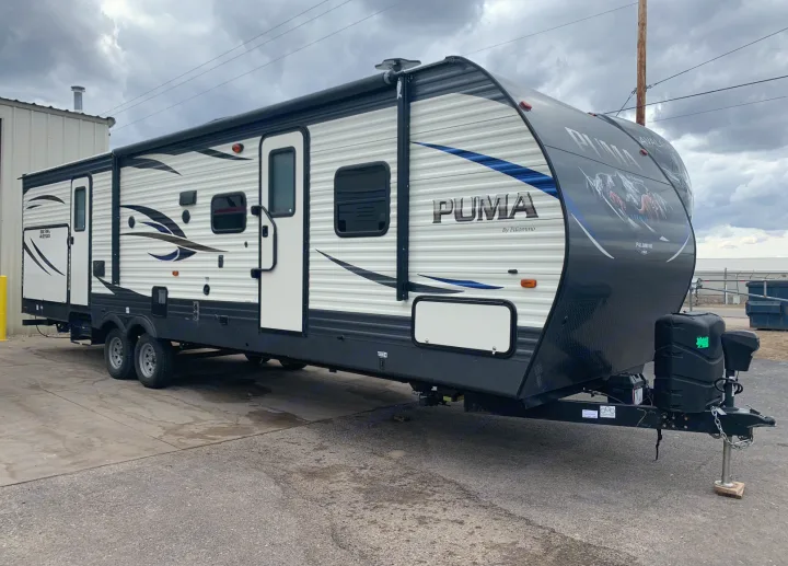 A white and black PUMA travel trailer by Palomino, a prime rv rental option, parked on asphalt.. Palomino Puma 2018