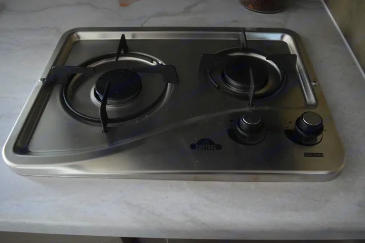 Inside an RV rental: a compact, two-burner stainless steel gas cooktop, with black grates and knobs.. Forest River X-Lite 2020