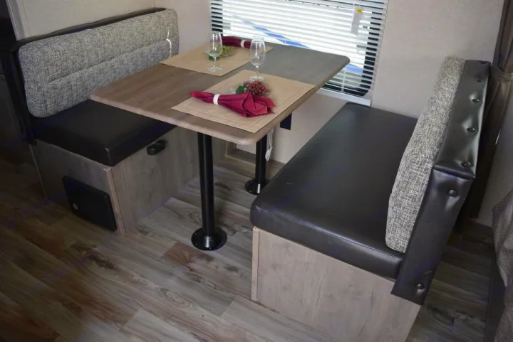 Inside an RV rental: a functional dinette with dark booth seating, a wood-look table, and matching flooring.. Forest River X-Lite 2020