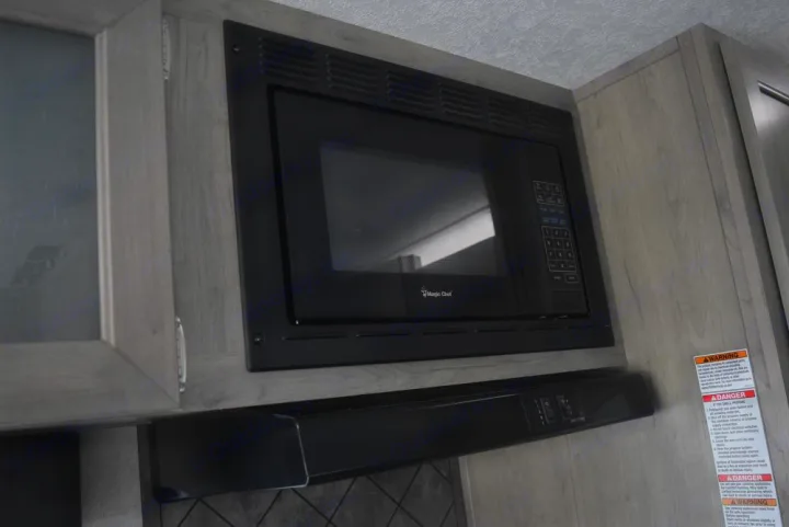 Modern RV rental kitchen appliances: a black Magic Chef microwave and range hood installed in light wood cabinetry.. Forest River X-Lite 2020