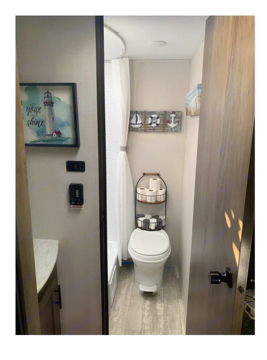 RV rental bathroom interior showcasing toilet, shower, vanity, and coastal decor including a lighthouse print.. Prime Time Avenger 2021