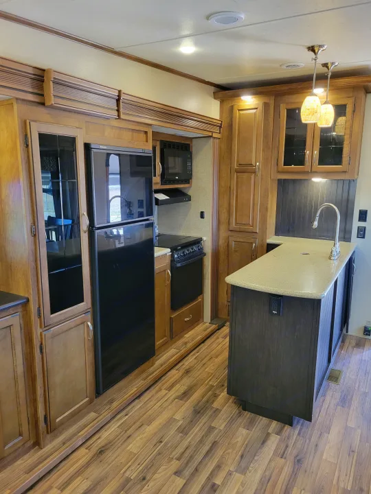 Modern RV kitchen with wood cabinets, black appliances, and island sink. Perfect for an rv rental experience.. Forest River Chaparral 2017