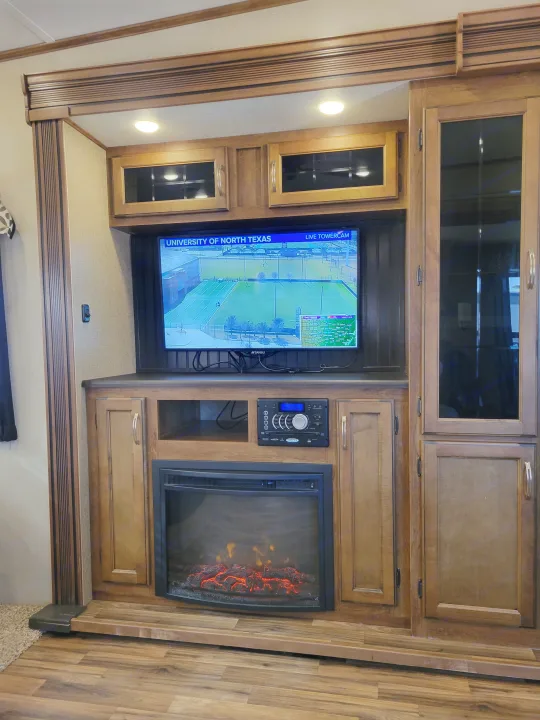 RV rental entertainment setup: TV displaying North Texas cam, electric fireplace, and stereo in a wood-paneled interior.. Forest River Chaparral 2017