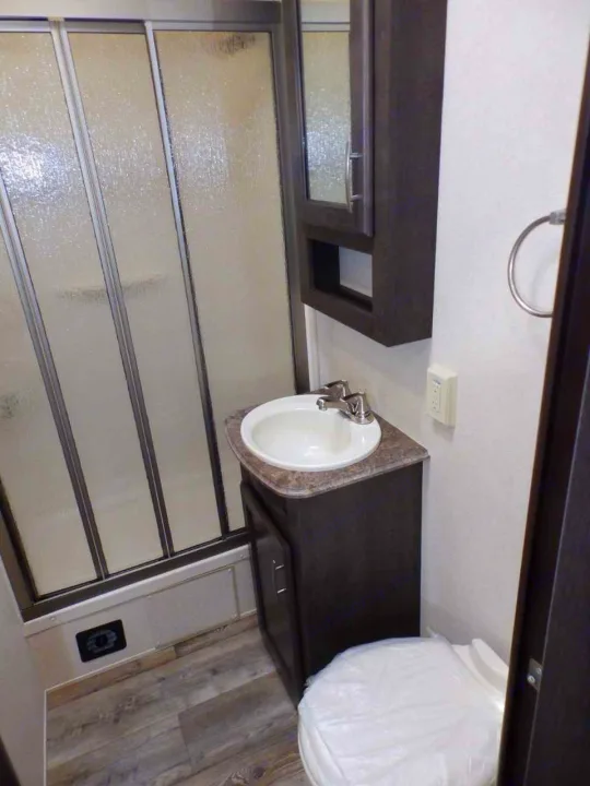 RV rental bathroom with shower, sink vanity, mirrored cabinet, and toilet. Compact interior for travel.. Forest River 211SLC 2018