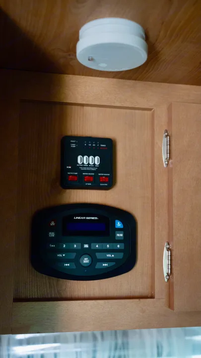 RV rental interior showing tank and water heater controls, a stereo system, and a ceiling-mounted smoke detector.. Old School 818 2021