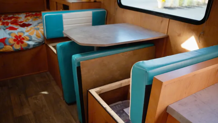 Cozy RV rental interior featuring a convertible dinette with blue benches, wood paneling, and storage. Perfect for travel.. Old School 818 2021