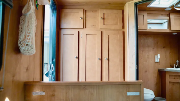 Inside an RV rental, light wood cabinets provide ample storage, leading to a compact bathroom with a toilet and sink.. Old School 818 2021