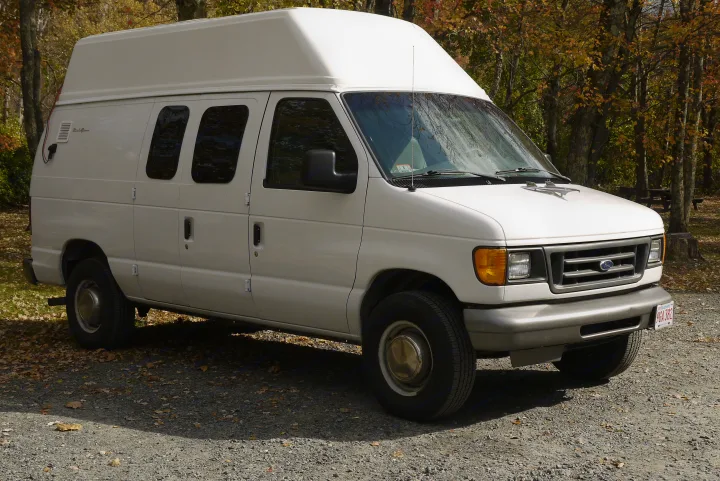 White high-top Ford RV rental van parked on gravel in autumn, ready for adventure.. Ford E350 Box Van 2003