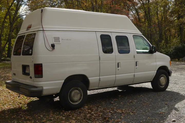 A white high-top Ford Econoline camper van, suitable for an rv rental, parked on a gravel path with autumn leaves.. Ford E350 Box Van 2003