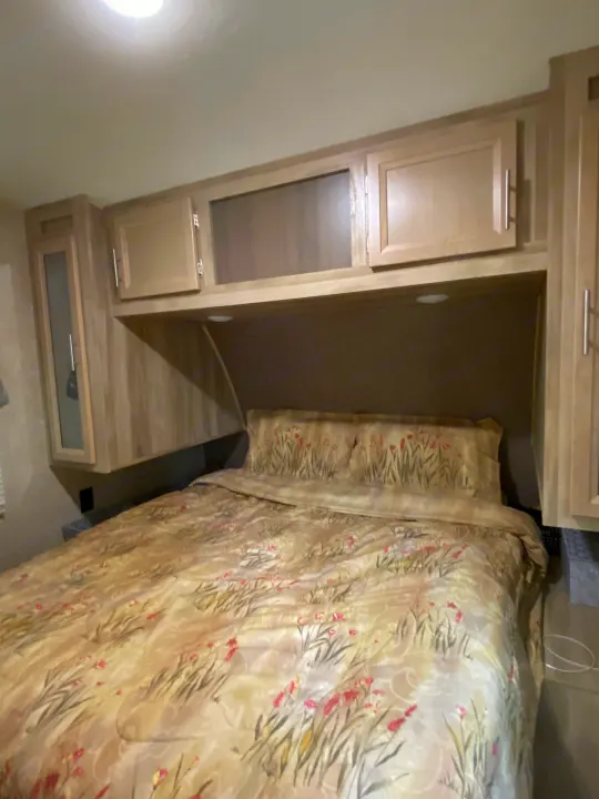 RV rental: Cozy bedroom with bed, floral bedding, and light wood overhead cabinets, some with glass inserts.. Forest River Coachmen Catalina Destination 2019