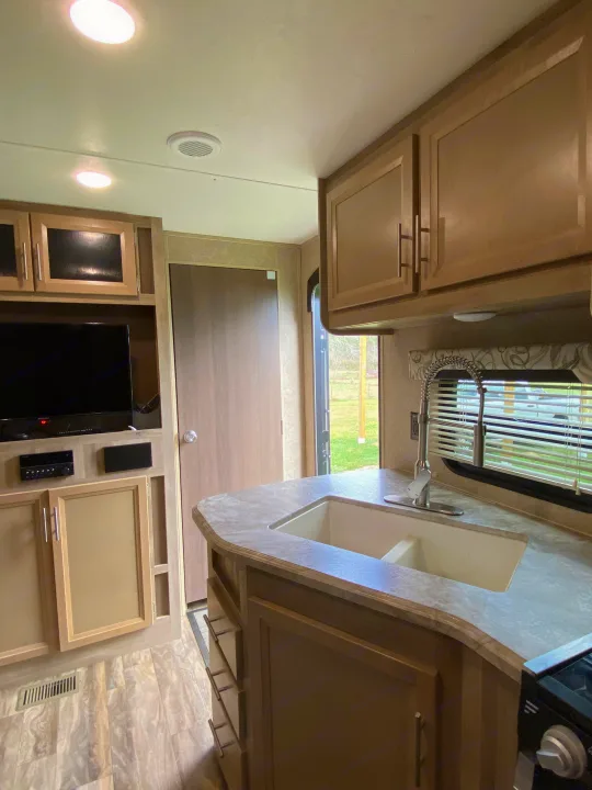 Bright rv rental interior featuring a compact kitchen with sink, light wood cabinets, and a living area with TV.. Forest River Coachmen Catalina Destination 2019