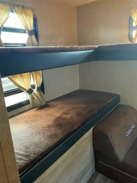 Inside an RV rental: brown bunk beds with textured mattresses and windows with light curtains, ideal for family trips.. Forest River Coachmen Catalina Destination 2019