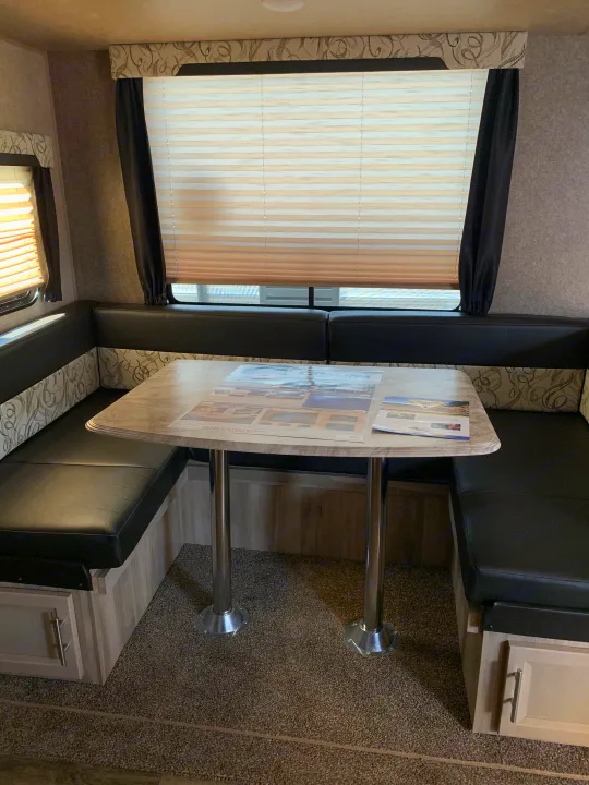 L-shaped dinette in an RV rental, featuring black seating, a light table, and window blinds.. Forest River Coachmen Catalina Destination 2019