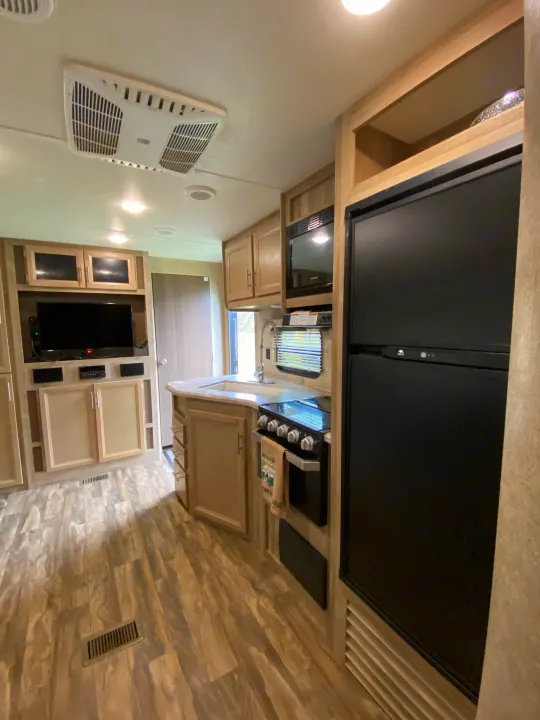 RV rental interior: A functional kitchen with fridge, stove, microwave, and sink, facing a TV entertainment unit.. Forest River Coachmen Catalina Destination 2019