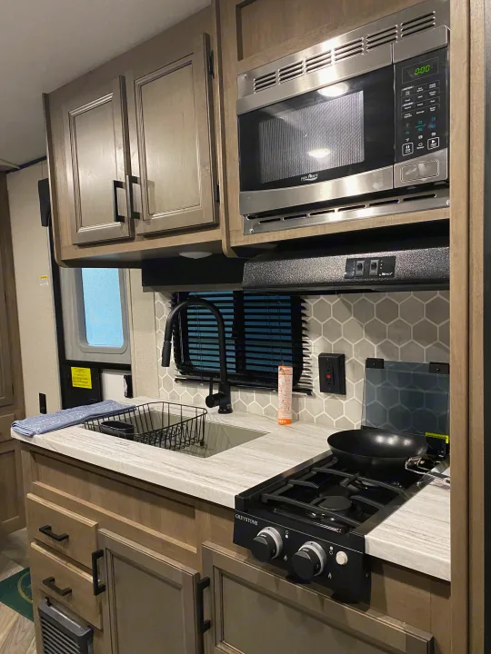 RV rental kitchen view with a High Pointe microwave, Greystone stovetop, sink, and honeycomb backsplash.. Highland ridge 19bh 2022