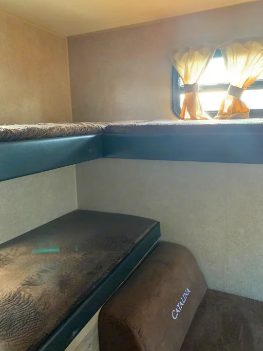 RV rental: view of stacked bunk beds. Upper bunk by a sunlit window; lower bunk shows a 'CATALINA' cushion.. Forest River Coachmen Catalina Destination 2019