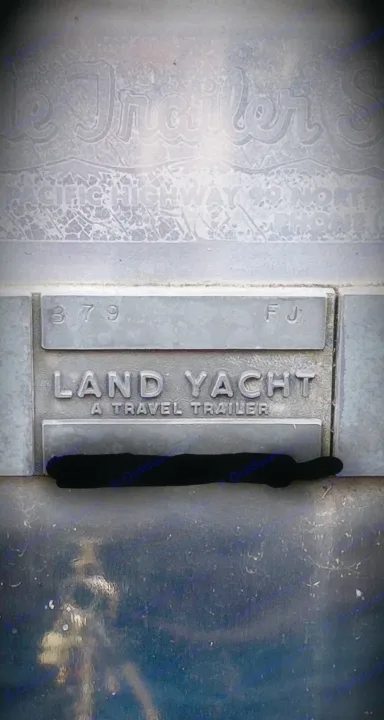 A distressed metal emblem reads "LAND YACHT A TRAVEL TRAILER," showcasing a classic RV available for rental.. Airstream Overlander 1969
