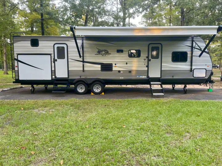 Jay Flight SLX travel trailer, ideal for an rv rental getaway. Parked in a wooded campsite with awning extended.. Jayco Jay Flight SLX 2021