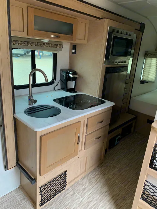 Inside an RV rental, a well-equipped compact kitchenette: sink, stovetop, microwave, fridge, and storage.. Forest River R-Pod 2020