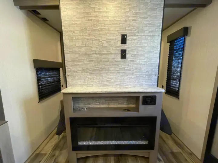 Modern RV rental living space featuring a faux stone media wall, electric fireplace, and windows with blinds.. Coleman Lantern 300tq 2022