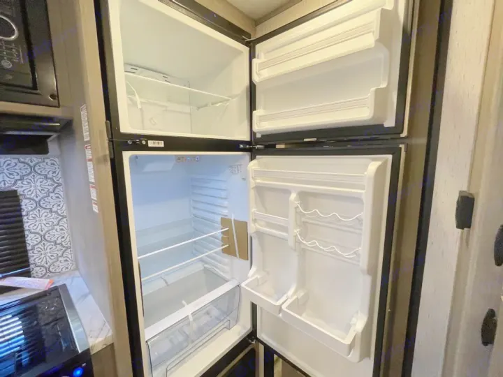 This RV rental features a clean, empty refrigerator and freezer, showing its spacious interior and shelves.. Coleman Lantern 300tq 2022