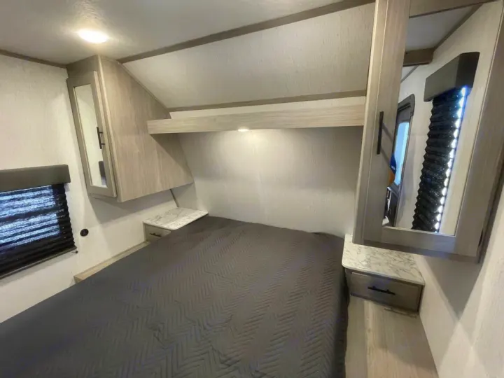 Inside this RV rental, a comfy bedroom features a large bed, overhead storage cabinets, nightstands, and window blinds.. Coleman Lantern 300tq 2022