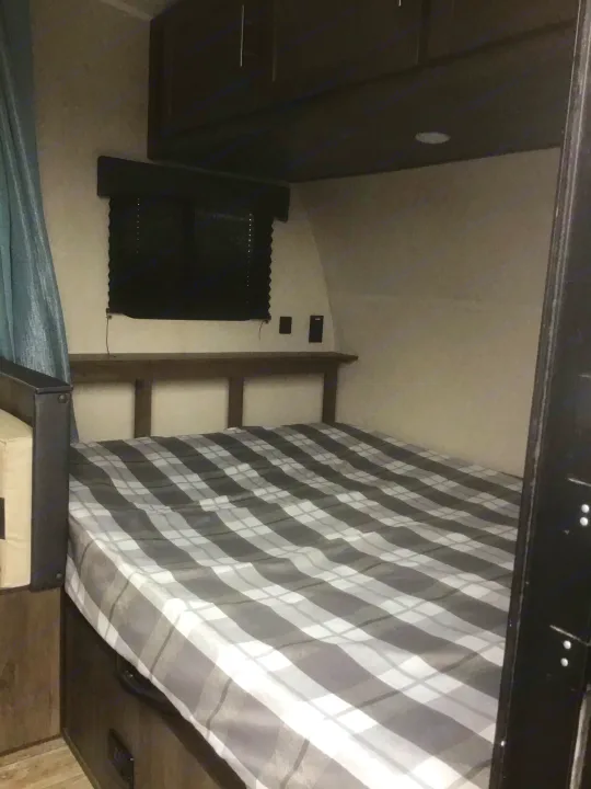 Cozy RV rental bedroom with plaid bedding, wood headboard, and overhead cabinets, ideal for your next trip.. Coachmen Clipper 2020